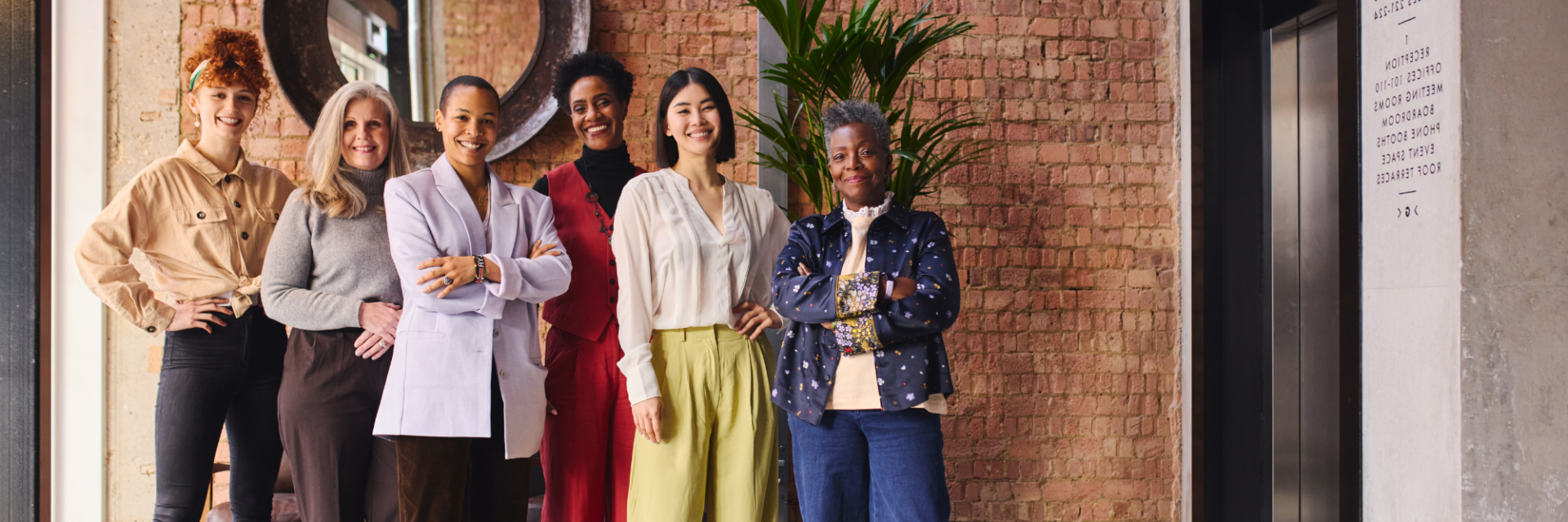 A group of diverse women in a modern office look triumphantly at camera